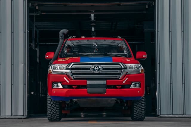 The front of a large, red, Toyota landcruiser by a grage